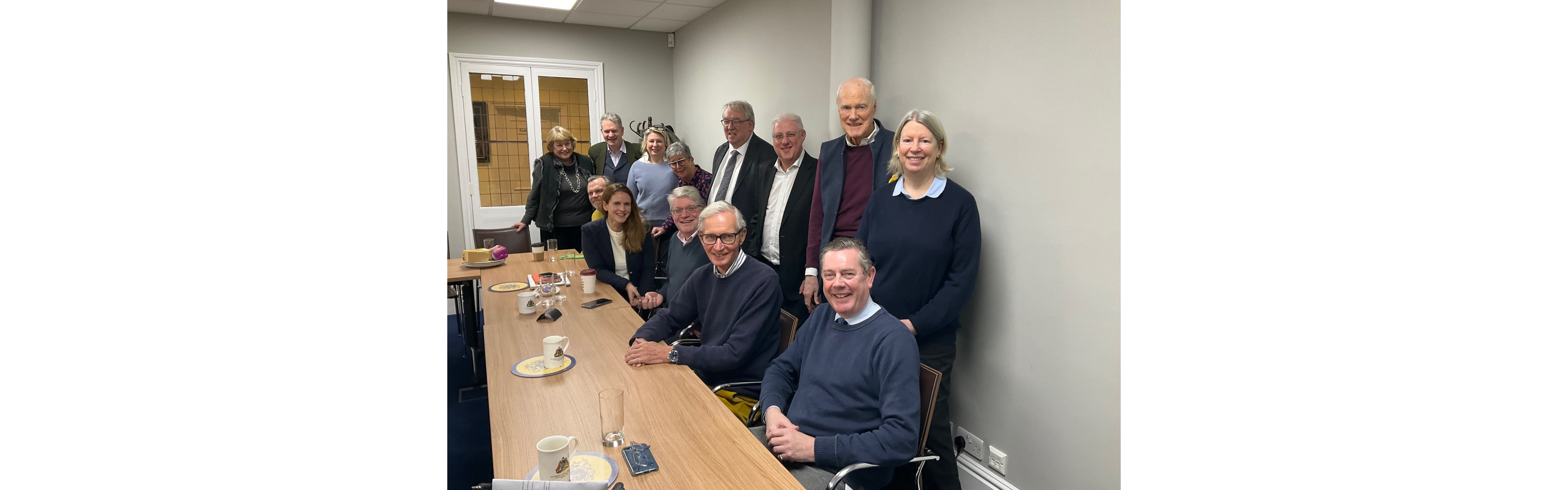 13 members of the Court working together. Pictured seated at meeting table and smiling. 