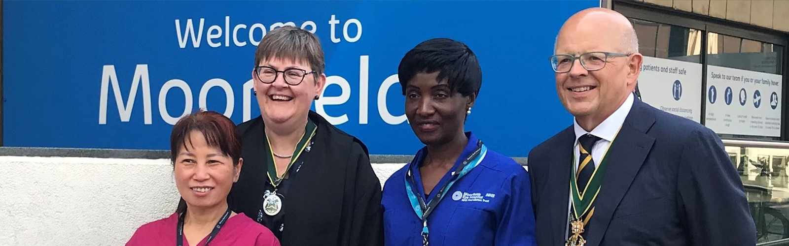 Image shows the Company Master and Clerk outside the entrance to Moorfields Eye Hospital, welcoming two nurse specialists as members of the Company. One nurse was born in Uganda, the other in China. Both have worked in the UK for over 20 years.